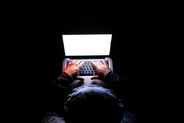A person in a dark room typing on a laptop, symbolizing privacy, cybersecurity, and technology.